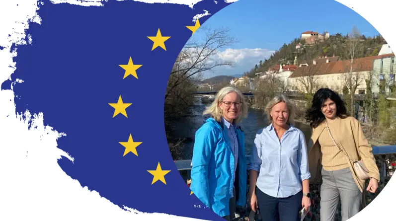 Bild på tre kvinnor. I bakgrunden syns EU-flaggan,  en å samt staden Graz.